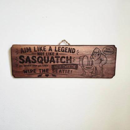 Finished laser-engraved walnut Sasquatch bathroom sign hanging on a white wall